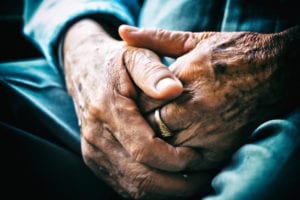 Senior man sitting on chair and cross arms. The image is a close up of his old and wrinkly hands. Prime candidate for hand rejuvenation